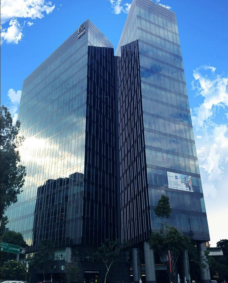 Exterior view of the glass-facade Prisma Insurgentes building under a blue sky.