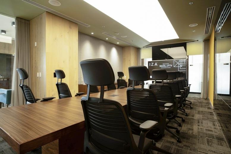 Close-up of a boardroom table and chairs with a presentation screen in the background.