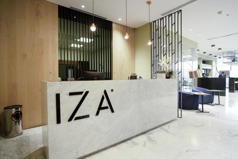 Bright marble-floored reception area with a sleek white front desk featuring the IZA logo.