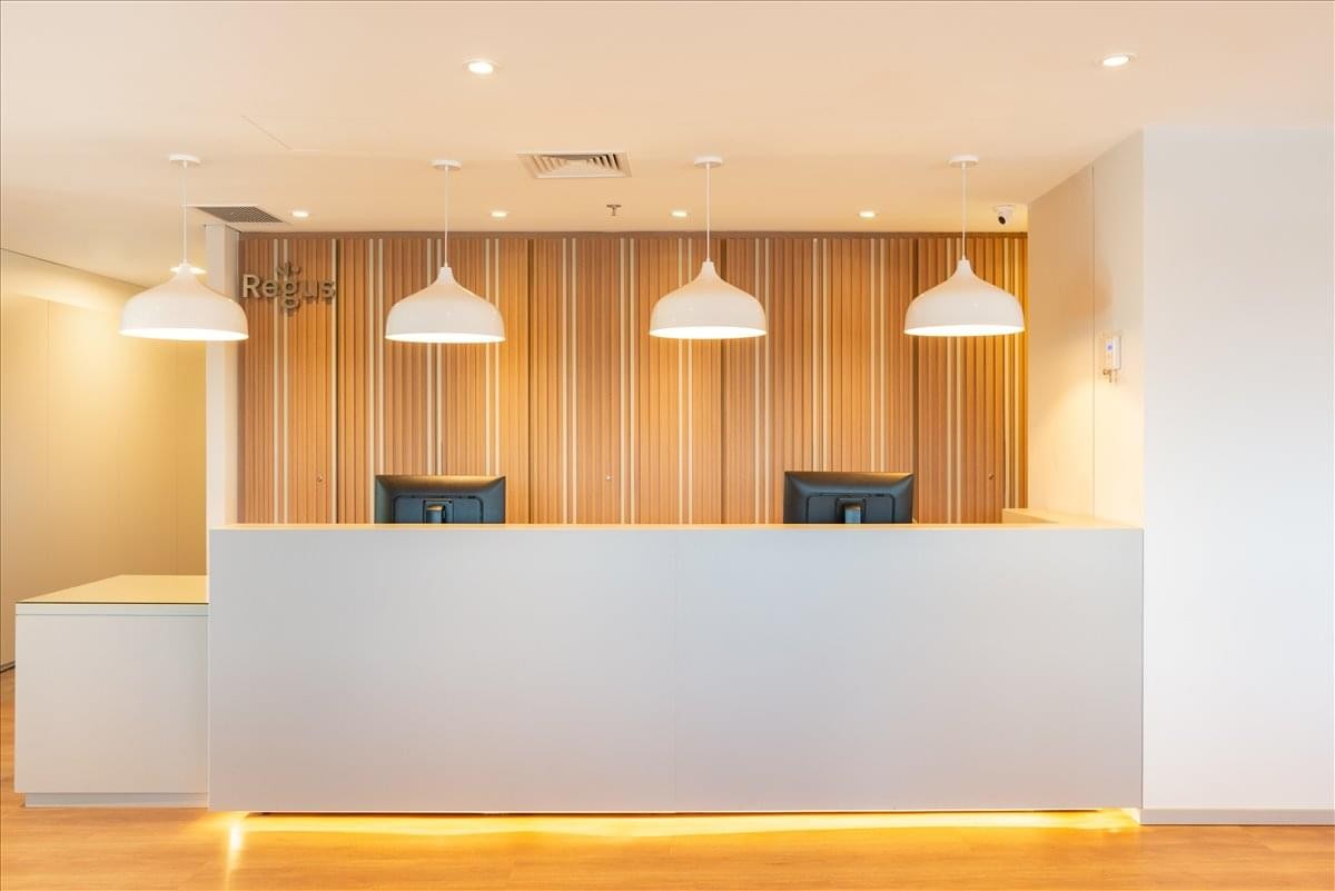 Modern minimalist reception desk with warm wooden wall paneling and pendant lighting.