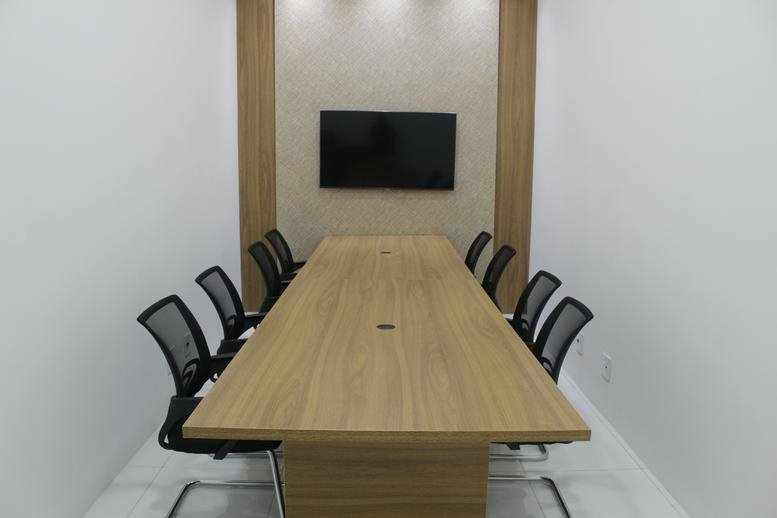 Meeting room at Rua Argolino de Morães, 87, with a long wood-tone table, black mesh chairs, and a wall-mounted screen.