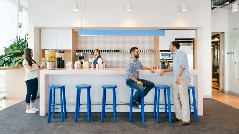 Communal break area with a white bar, blue stools, and people socializing at Reforma 26.