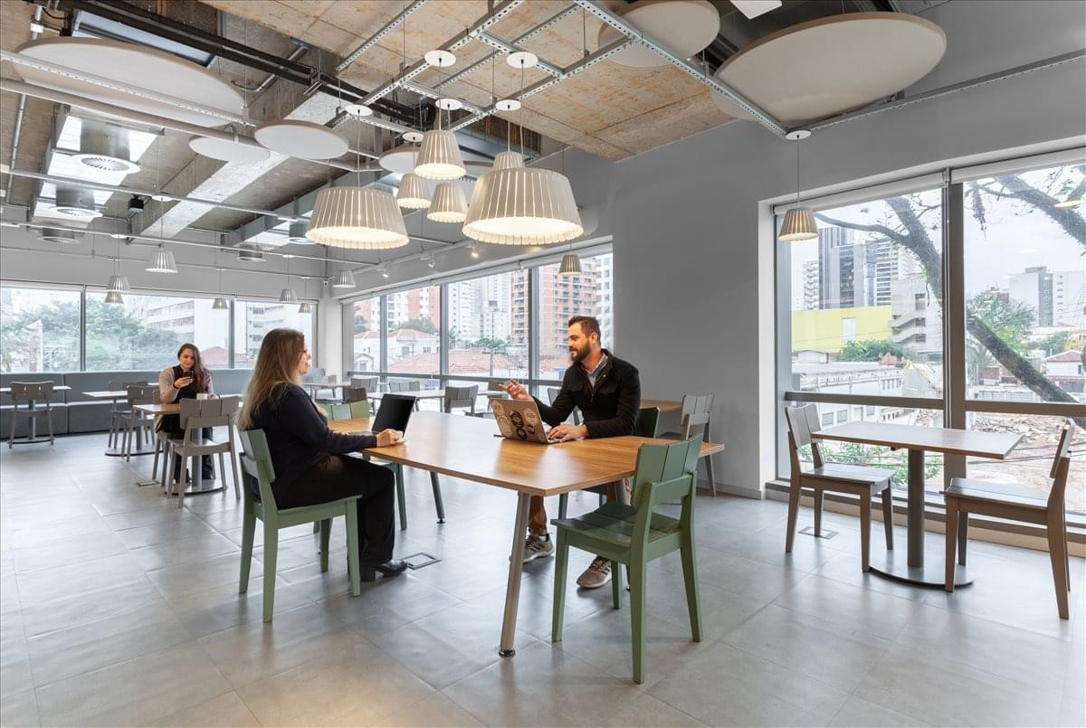 Professional interior of the Spaces Villa Madalena with natural light and long wooden coworking tables.