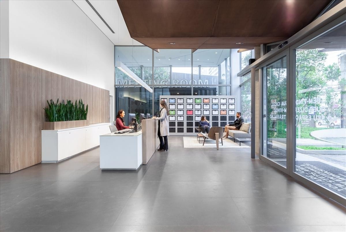 Modern lobby at Spaces Villa Madalena with wooden reception desk and indoor plants.