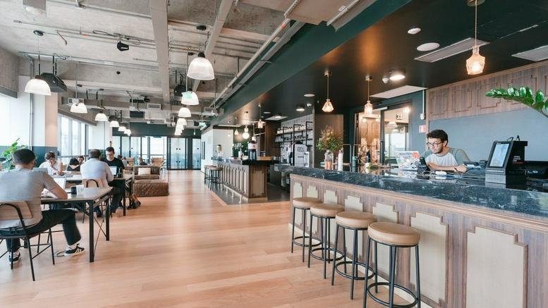 Spacious communal lounge and cafe at Torre JK with industrial ceilings and warm wood flooring.