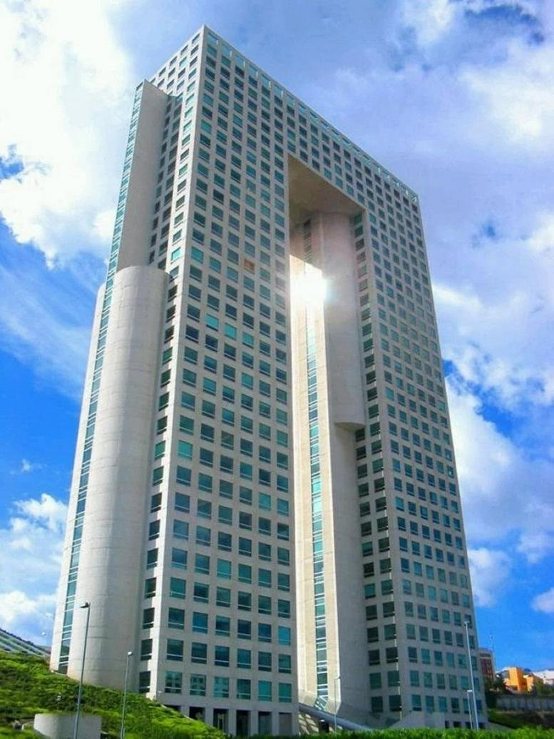 The striking architectural arch facade of Tower A, Paseo de Los Tamrindos, Mexico City under a blue sky.