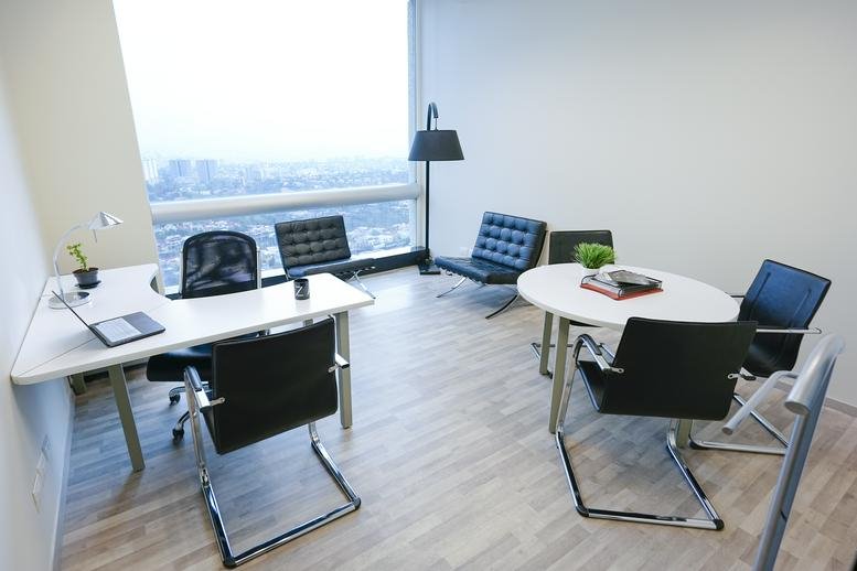 Well-lit office area with a curved desk, lounge seating, and an expansive city view.