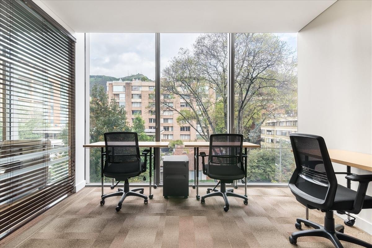 Bright shared office space with black mesh chairs and views of the Urban Plaza Building exterior.