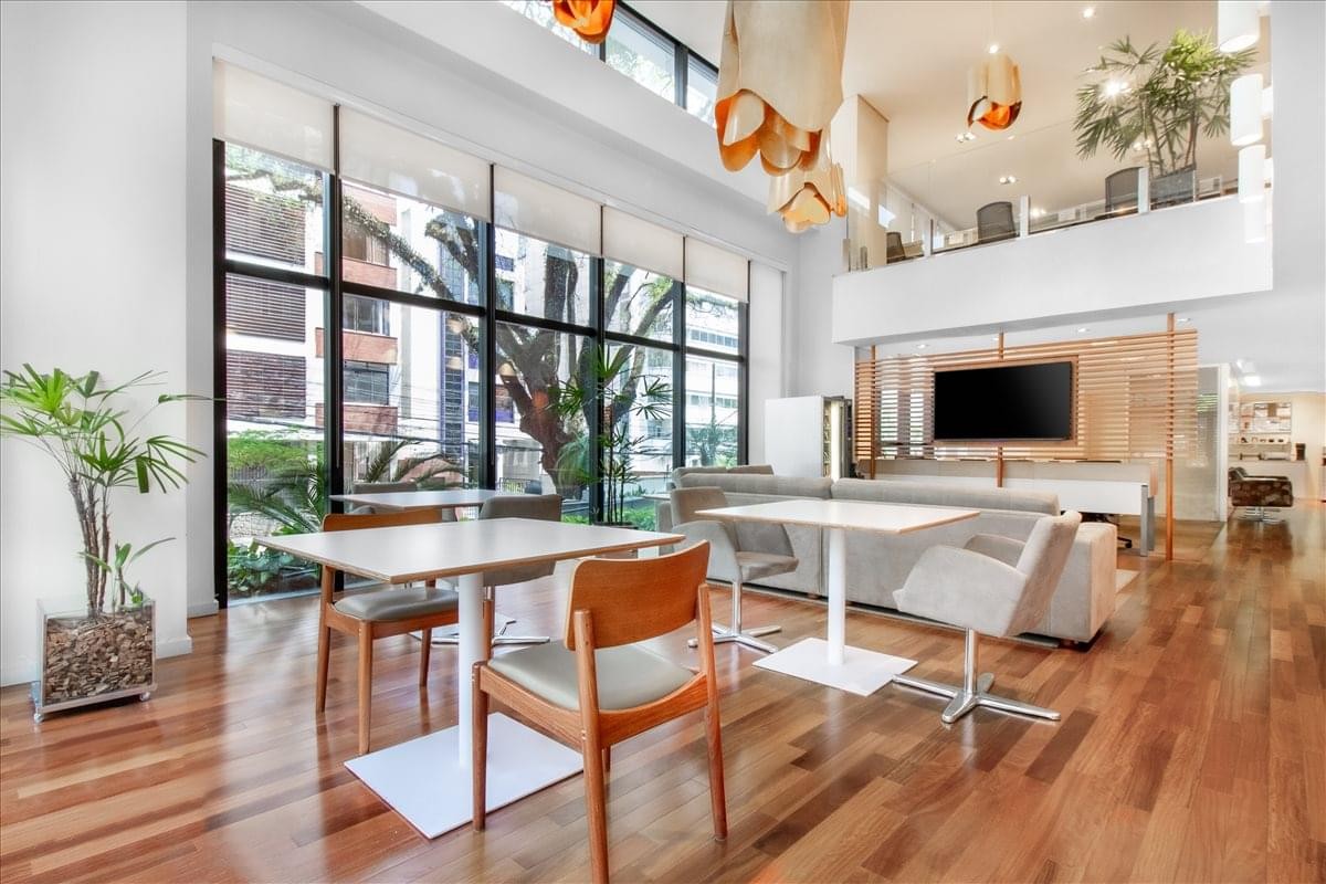 Bright double-height communal lounge with wooden floors, white tables, and designer lighting.
