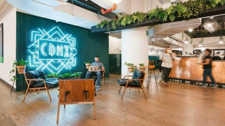 Spacious communal lounge at Montes Urales 424 featuring a neon logo wall and modern armchairs.