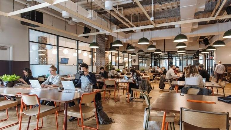 Large coworking hub with high ceilings, pendant lighting, and various communal tables.