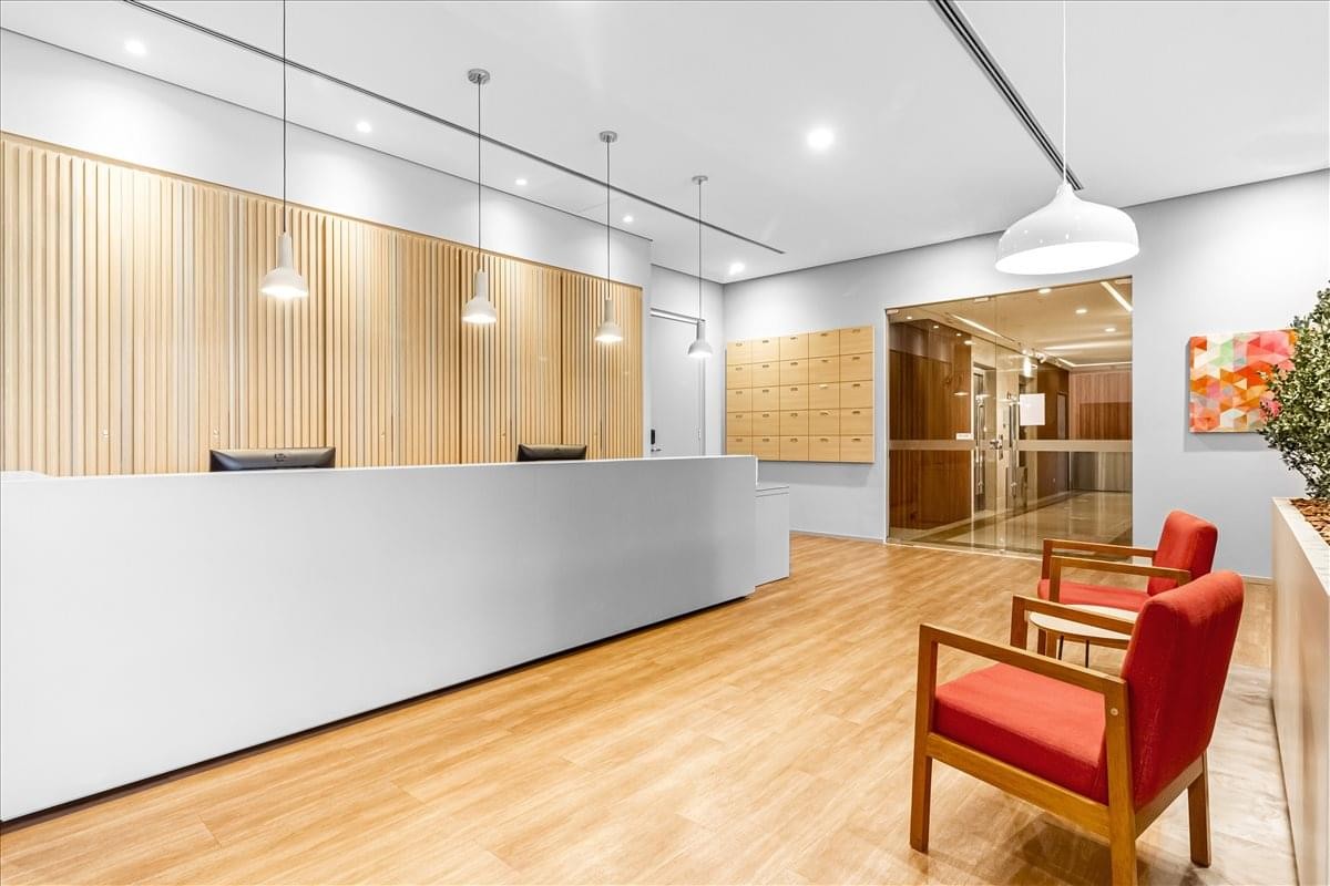 Bright reception area featuring a white front desk, wooden wall panels, and red accent chairs.
