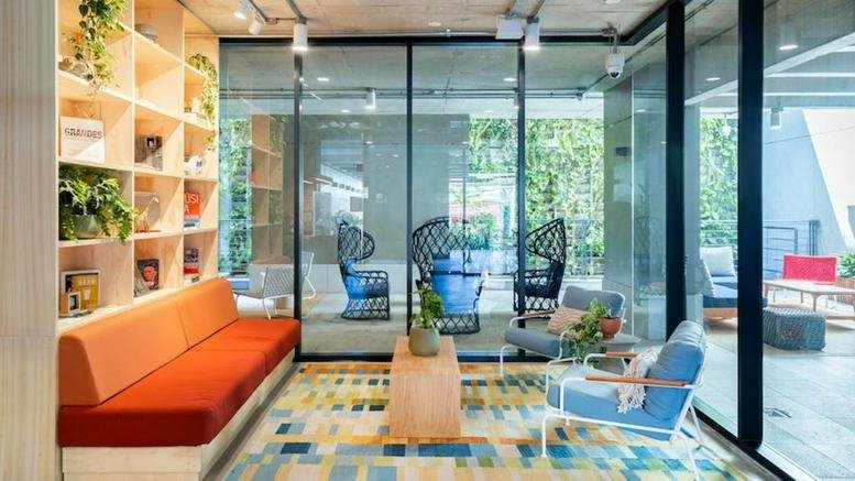 Lounge area with an orange sofa, colorful rug, and floor-to-ceiling glass walls at Rua Purpurina 400.