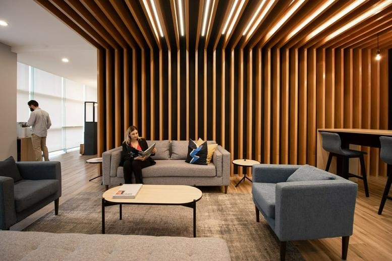 Lounge at Semillero Obispado featuring a stylish wooden slat wall, gray sofas, and modern blue armchairs.