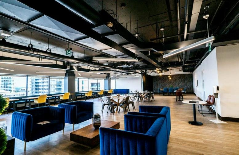 Spacious communal lounge with blue velvet sofas, modern lighting, and expansive window views.