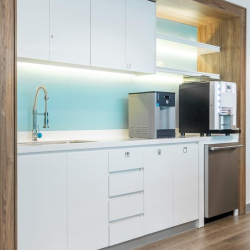 Modern office kitchenette with white cabinetry, a glass backsplash, and coffee machines.