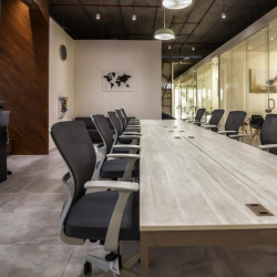 Perspective view of a long communal workspace and gray mesh office chairs.