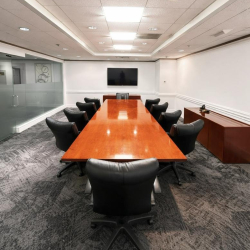 Conference room with a long polished wooden table and black leather chairs.