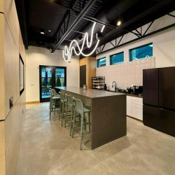 Kitchen breakroom with a grey breakfast bar, green stools, and black fridge.