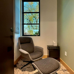 Small private room with a grey armchair and ottoman beside a window.