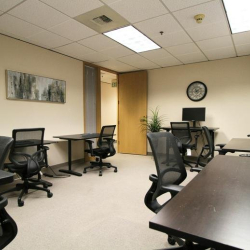 Shared office area with individual desks, mesh chairs, and a wall clock.