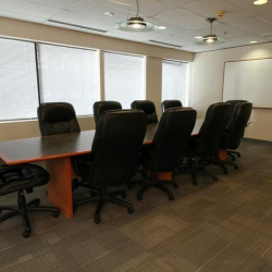 Spacious boardroom featuring a long wooden table and executive black leather chairs.