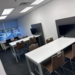 Coworking area with high-top desks, integrated monitors, and grey privacy screens.