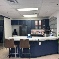 Modern office kitchenette with navy blue cabinets, white counters, and a breakfast bar.