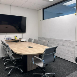 Small professional meeting room with an oval wooden table and large wall-mounted screen.