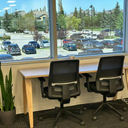 Shared desk space by a large window overlooking a parking area and trees.