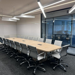 Large conference room with a long wood table, grey chairs, and glass partition walls.