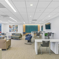 Large training room with rows of grey tables, ergonomic chairs, and wall-mounted presentation screens.