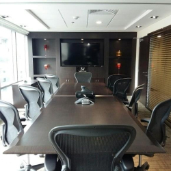Formal boardroom with a long dark conference table, ergonomic mesh chairs, and integrated media screen.