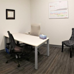 Compact internal office with a white desk, black chairs, and framed art.