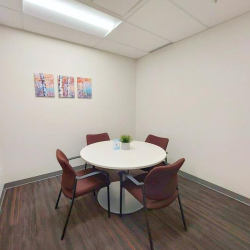Small meeting room with a round white table and four maroon chairs.
