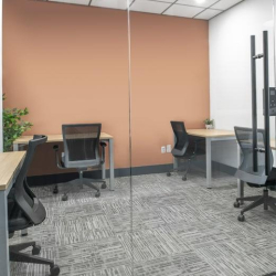 Shared three-person office suite with a warm orange accent wall and glass partition.