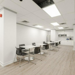 Modern lunchroom with white tables, black chairs, and a white kitchenette.