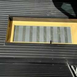 Small window with striped horizontal blinds set in a corrugated wall.