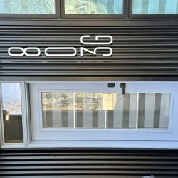 Building address 803G mounted on dark corrugated metal siding.