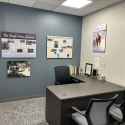 Private office featuring an L-shaped desk and a blue accent wall with framed posters.