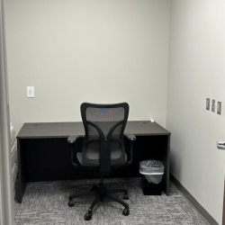 Minimalist private office with a dark desk, mesh chair, and neutral walls.