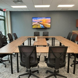 Large boardroom with a U-shaped wooden table, mesh chairs, and a wall-mounted TV.