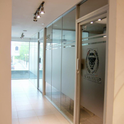 Bright office corridor featuring glass-walled suites and frosted door logos.