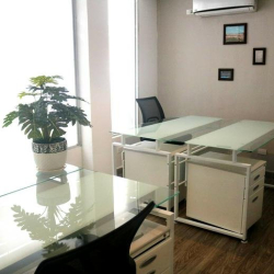 Bright shared workspace with white storage cabinets and glass desks near a window.