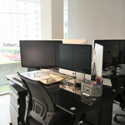 Modern workstation setup with dual monitors on a black glass desk and mesh chair.