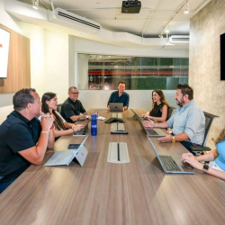 Bright conference room with people seated around a long wooden table.