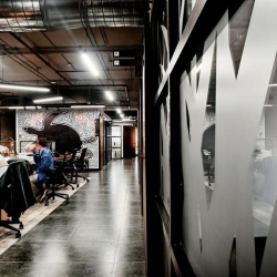 Modern office corridor with frosted glass partitions and people working at collaborative desks.