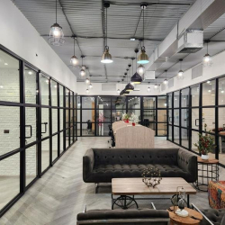 Spacious lounge area with a tufted grey sofa, modern lighting, and glass office partitions.