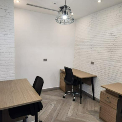 Minimalist office space with wooden desks and black task chairs against white brick walls.