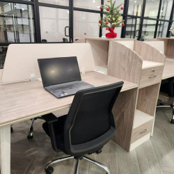 Modern coworking desks equipped with laptops and black task chairs near glass walls.